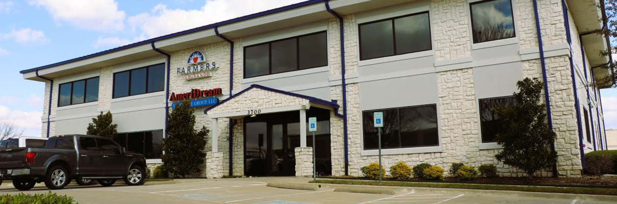 Two-story commercial office building with a light stone exterior, dark-framed windows, covered entrance, accessible parking spaces, landscaping, and tenant signage including Farmers Insurance and AmeriDream.