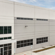 Exterior view of a modern commercial or industrial building at 4001, featuring a light gray facade, large windows, accessible entrances, and an adjacent parking area.