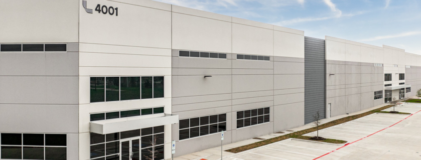 Exterior view of a modern commercial or industrial building at 4001, featuring a light gray facade, large windows, accessible entrances, and an adjacent parking area.