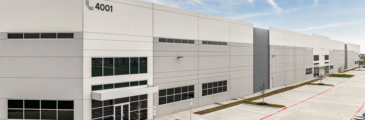 Exterior view of a modern commercial or industrial building at 4001, featuring a light gray facade, large windows, accessible entrances, and an adjacent parking area.