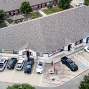 4819 SH121 Aerial view of a single-story commercial office building with a large gray roof, surrounding parking areas, accessible parking spaces, parked vehicles, mature trees, and neighboring buildings.