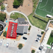 5809Windhaven Aerial view of a mixed-use entertainment and dining area with an available commercial space highlighted in red beside Turbo Coffee & Creative, near OMG Tacos, The Empanada Cookhouse, outdoor gathering areas, and adjacent soccer fields.