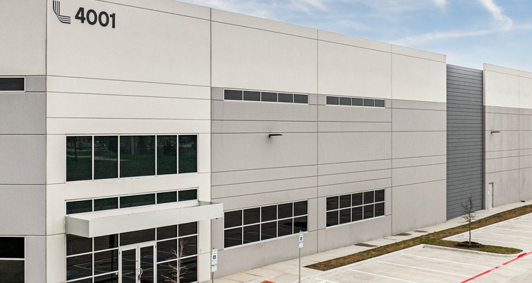 Exterior view of a modern commercial or industrial building at 4001, featuring a light gray facade, large windows, accessible entrances, and an adjacent parking area.