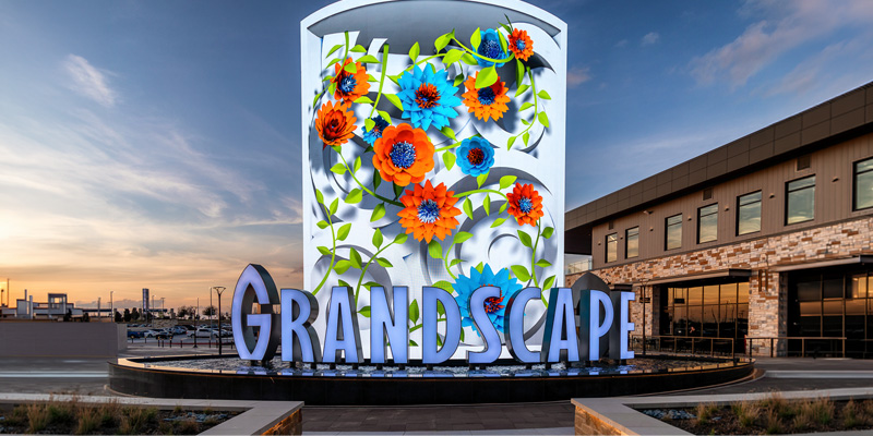 Grandscape monument sign featuring a colorful floral display, with large “GRANDSCAPE” lettering in front of surrounding retail and entertainment buildings.
